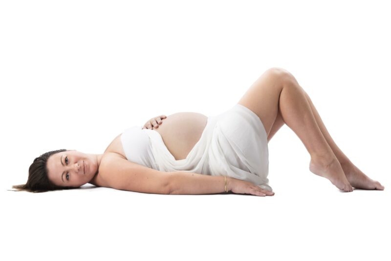 Portrait de femme enceinte en couleur en studio allongée sur le dos sur fond blanc pour Lorie Diaz Photographe
