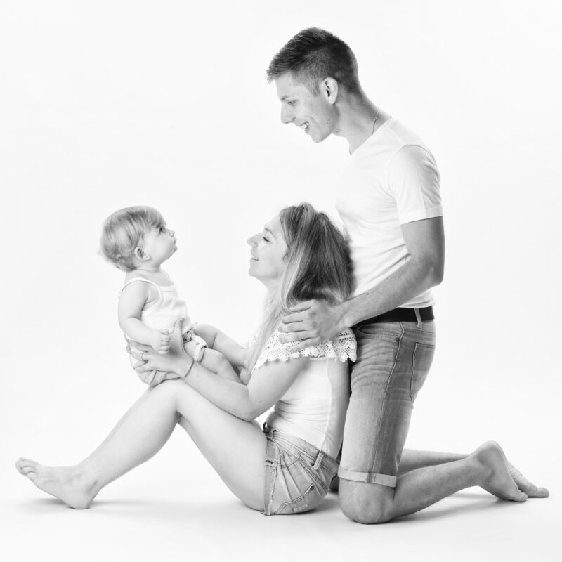 Photo de famille en studio en noir et blanc d'un couple avec leur enfant sur les genoux pour Lorie Diaz photographe