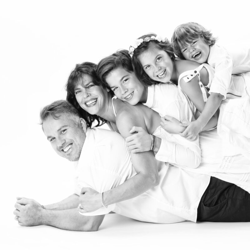 Photo de famille en studio en noir et blanc d'une famille avec un couple et leurs enfants allongés sur le dos les uns des autres pour Lorie Diaz photographe