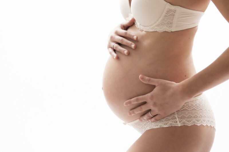 Photo d'un ventre de femme enceinte en lingerie blanche sur fond blanc en studio pour Lorie Diaz photographe