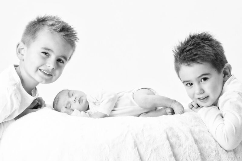 Portrait de famille et naissance en studio avec 2 enfants qui regardent l'objectif et un bébé qui dort sur un drap blanc pour Lorie Diaz Photographe à Saint Rémy-de-Provence
