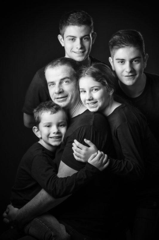 Photo de famille d'un père avec ses 4 enfants en noir et blanc en studio sur fond noir pour Lorie Diaz photographe