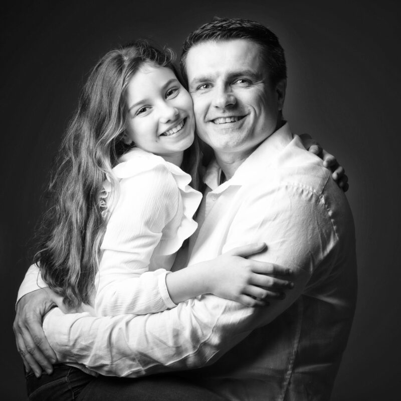 Portrait de famille d'une père et de sa fille dans ses bras en noir et blanc en studio sur fond noir pour Lorie Diaz photographe