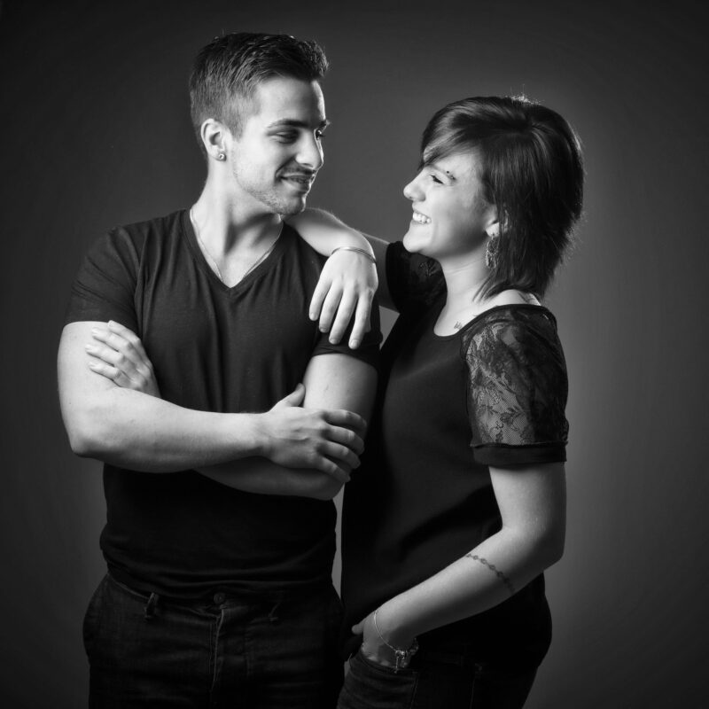 Portrait de famille d'un couple en noir et blanc sur fond gris pour Lorie Diaz photographe