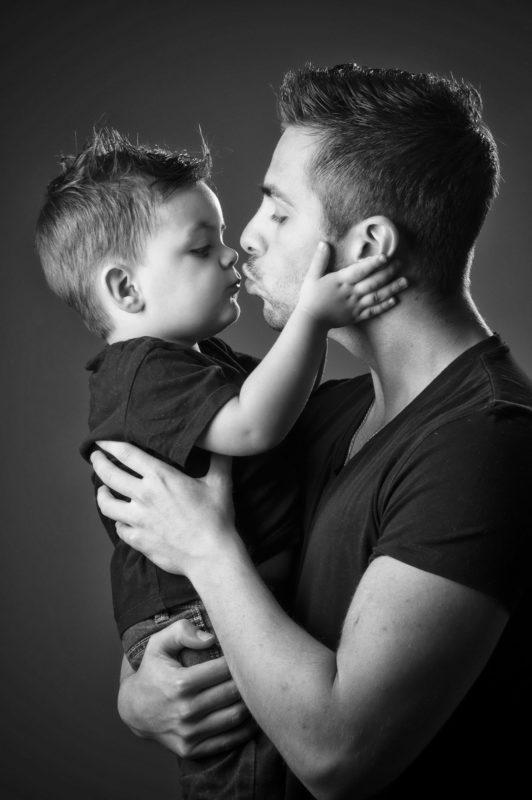 Portrait de famille en noir et blanc en studio sur fond gris d'un père avec son fils dans les bras pour Lorie Diaz photographe