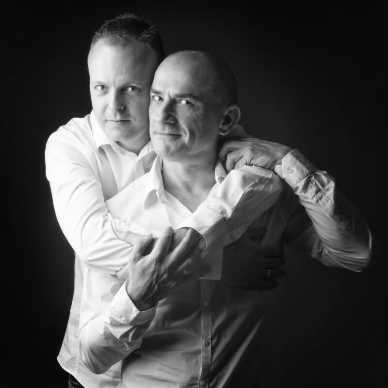 Portrait en noir et blanc en studio d'un couple d'hommes sur fond noir pour Lorie Diaz photographe